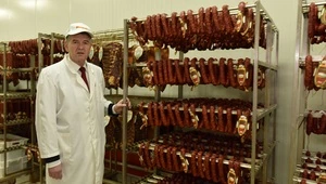 Petar Matijević standing in a meat processing facility surrounded by hanging sausages