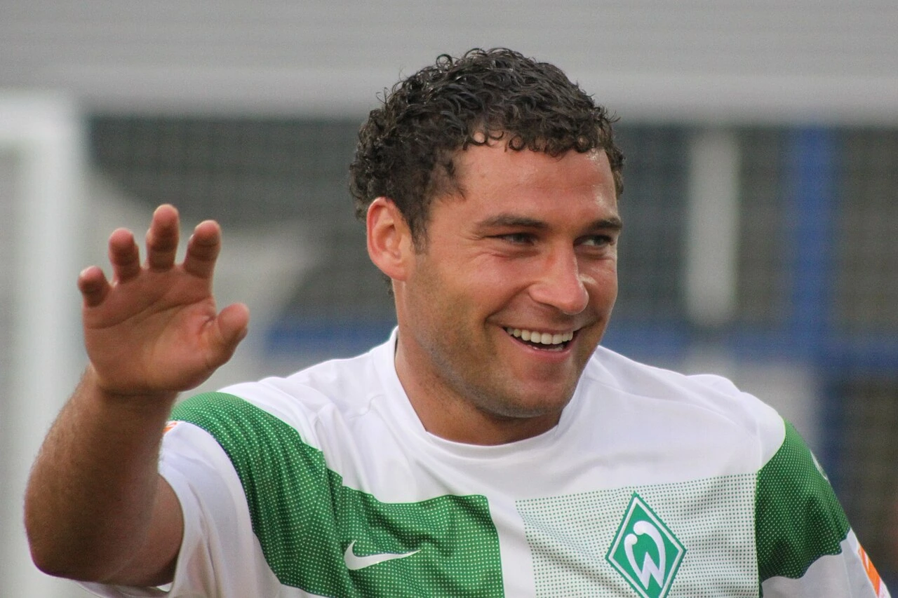 Duško Tošić in a Werder Bremen jersey, smiling and waving.
