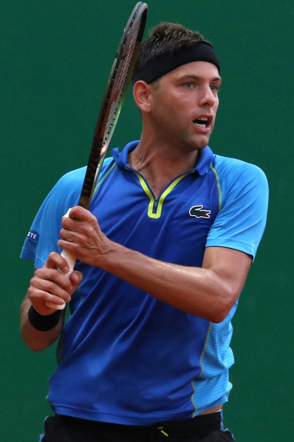 Filip Krajinović in action on the tennis court wearing a blue shirt and black headband, holding a racket.