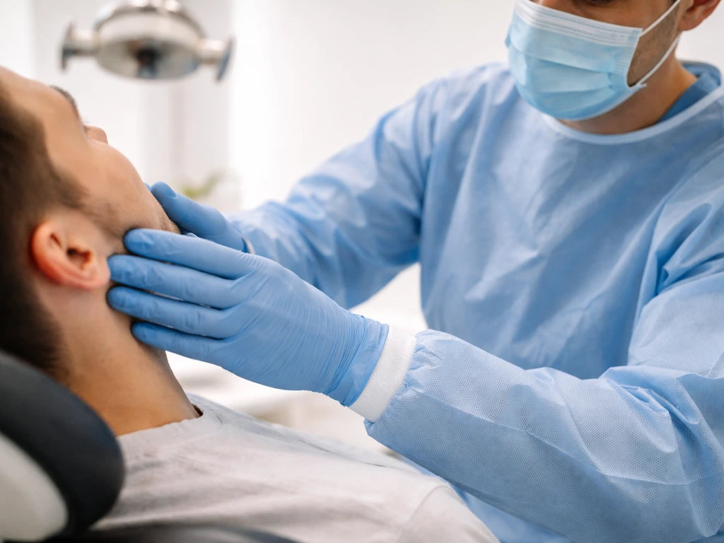 Dentist examining a patient’s jaw in a dental clinic exam room, focus on TMJ assessment.