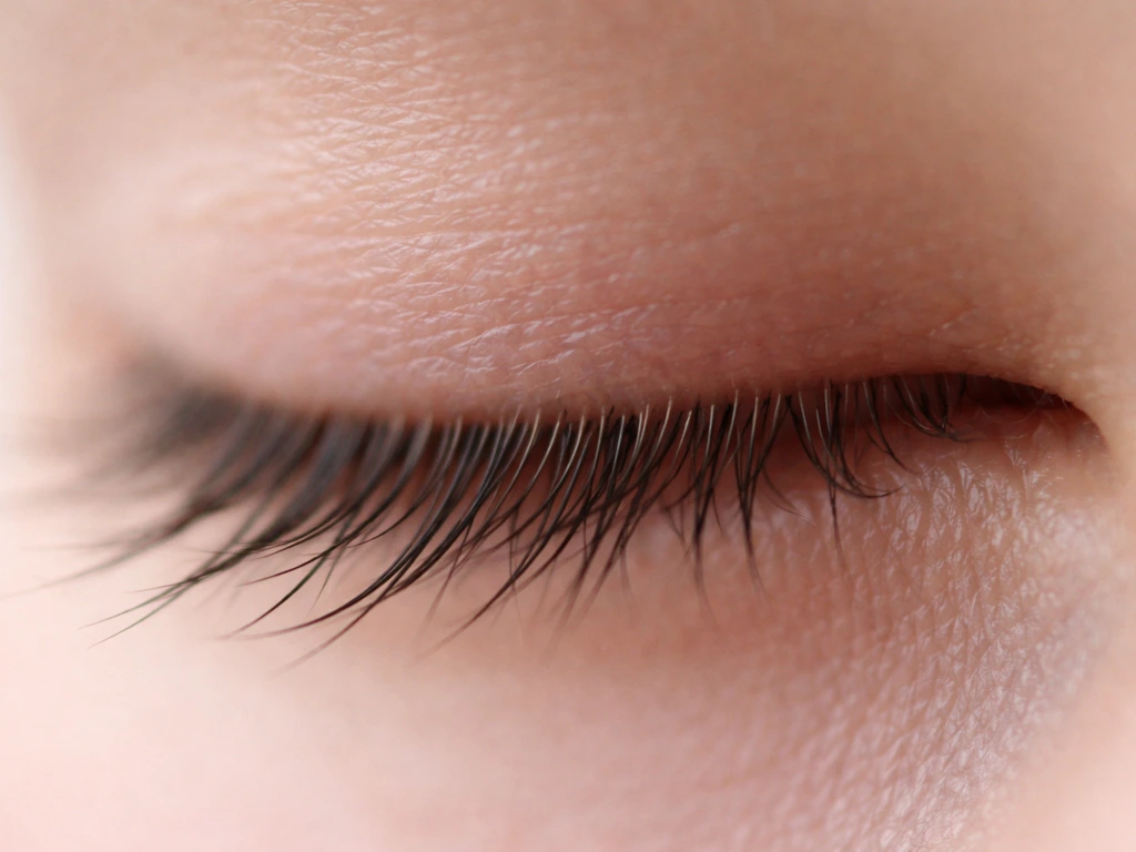 Macro close-up of an eyelash line showing lashes growing in different directions against a clean background.