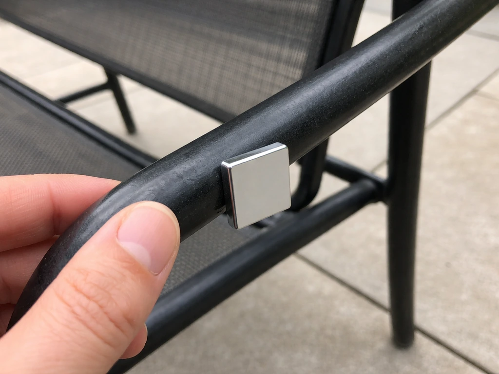 A hand holds a refrigerator magnet against a metal patio chair frame outdoors.