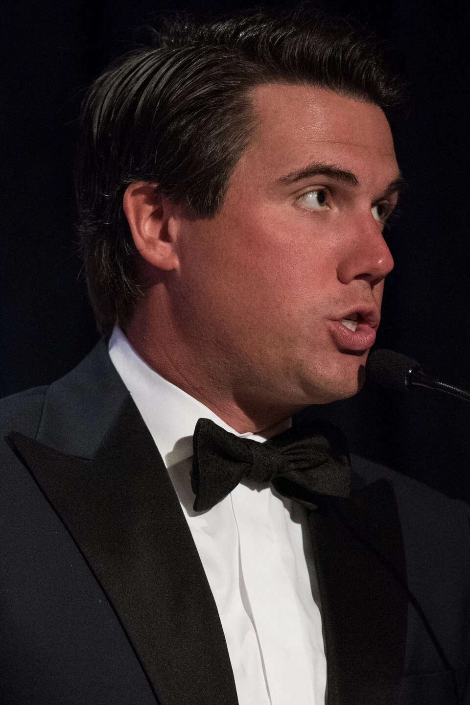 Broadcast journalist Leland Vittert speaking at a podium in a formal tuxedo