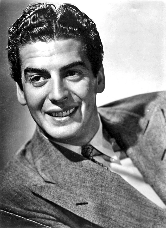 Black-and-white publicity portrait of Victor Mature in a suit, smiling toward the camera.