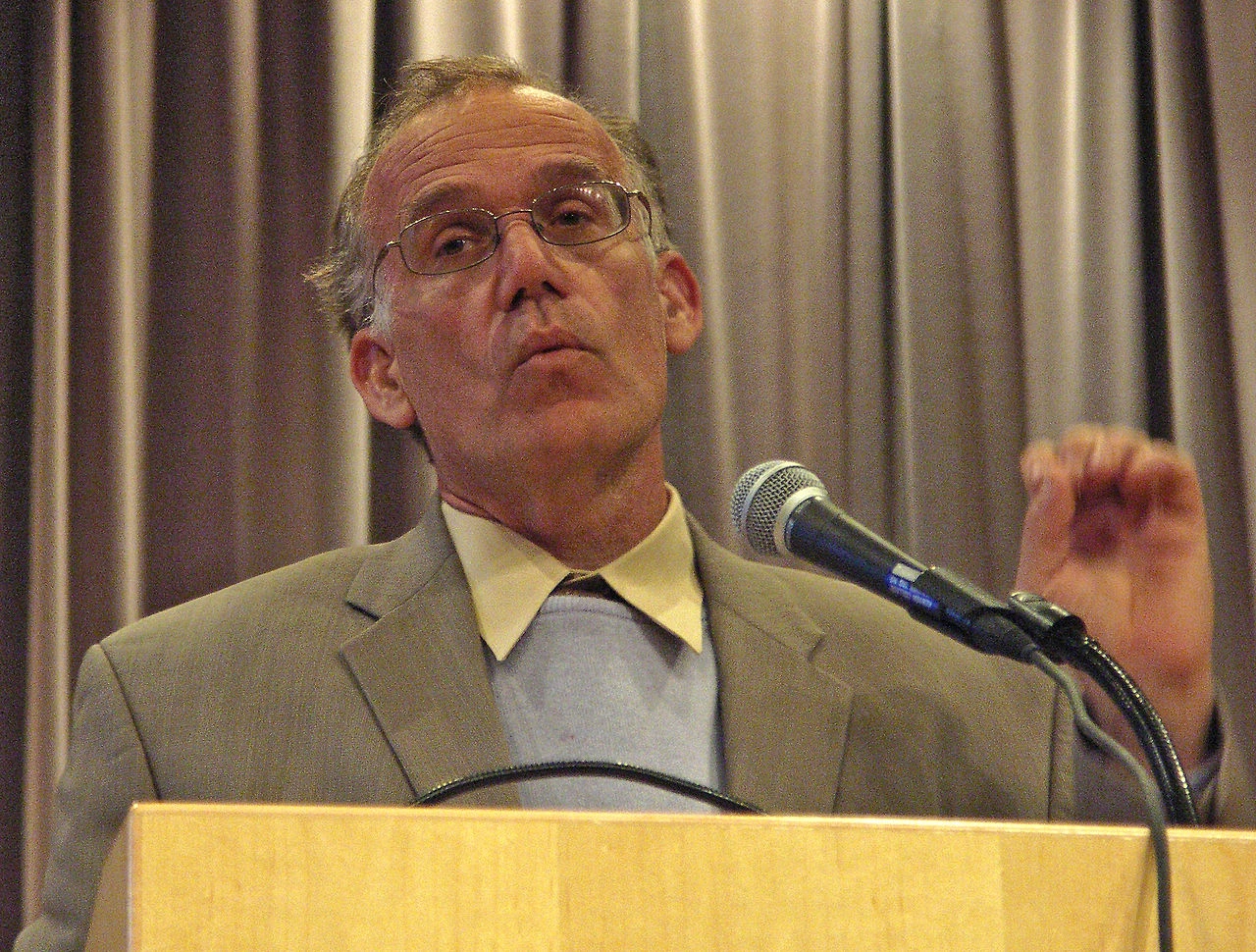 Victor Davis Hanson speaking at a podium with a microphone in front of curtains