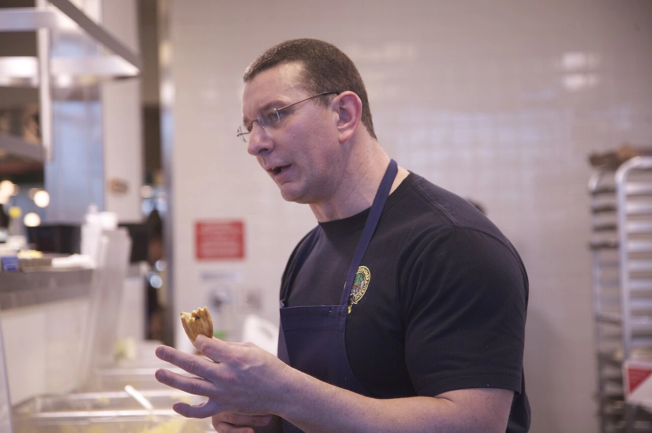 Chef Robert Irvine in a kitchen, holding food and wearing an apron