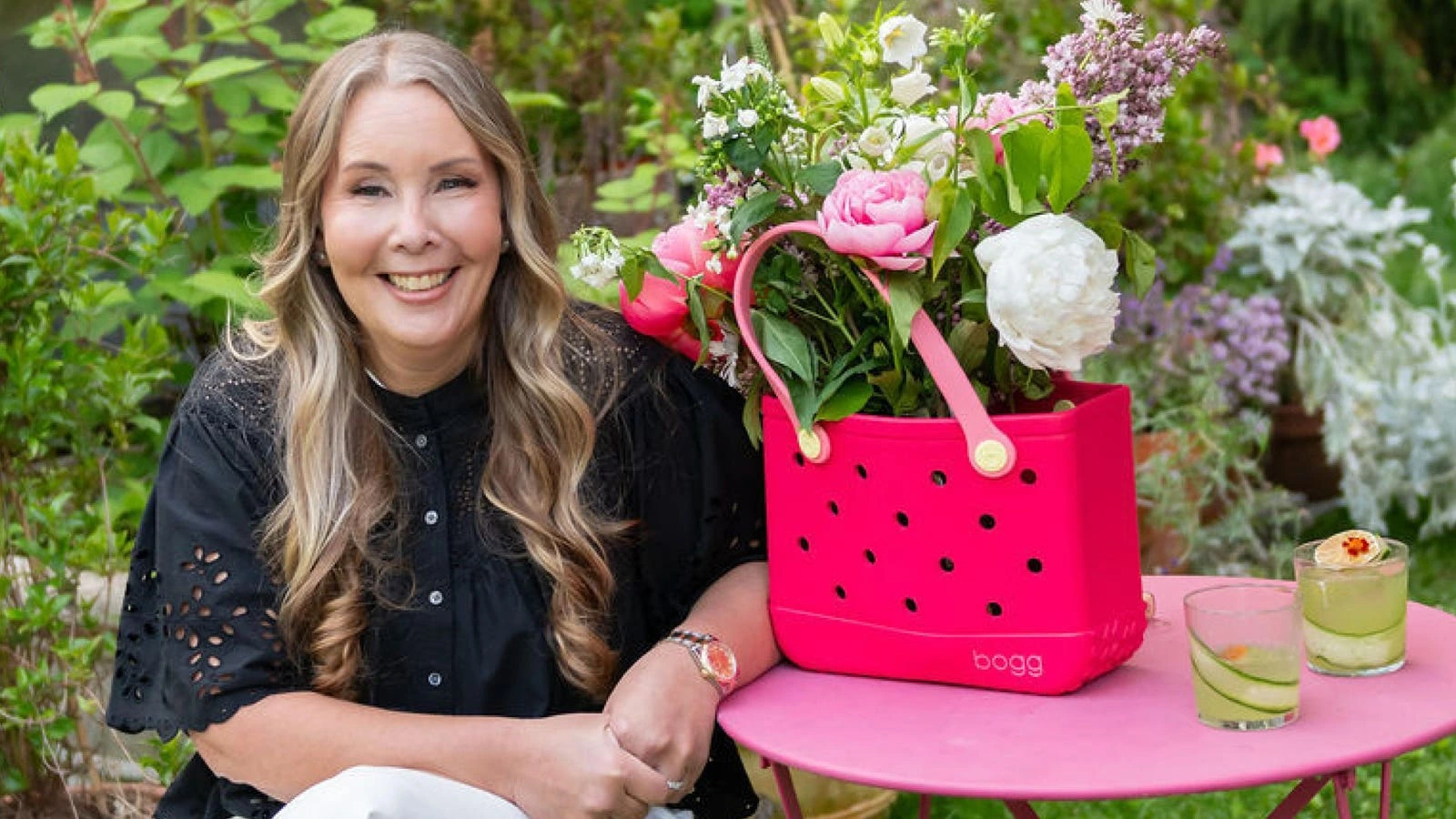 Kim Vaccarella smiling outdoors beside a bright pink Bogg tote filled with flowers