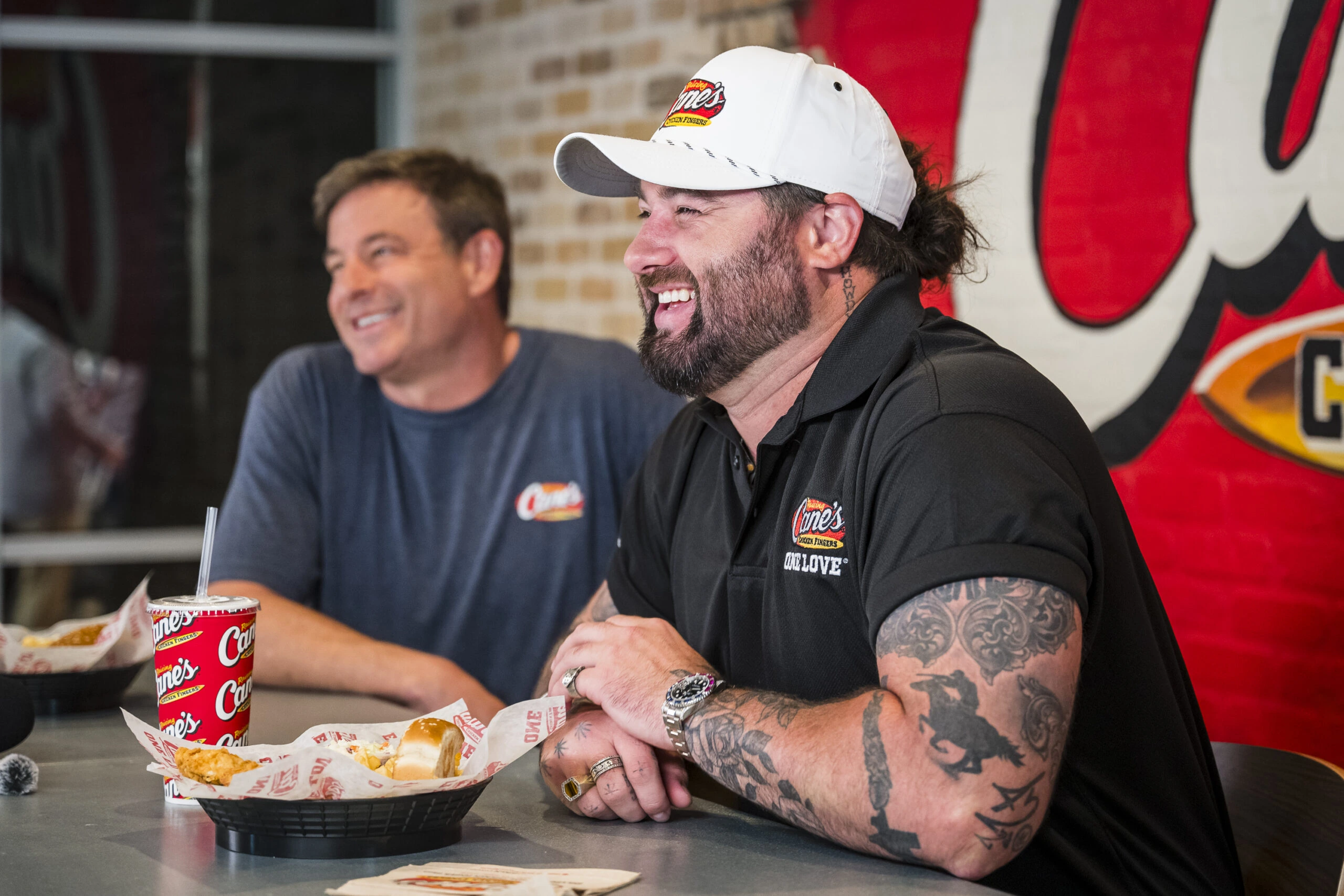 Koe Wetzel smiling at a Raising Cane's event, wearing a white cap and black polo shirt