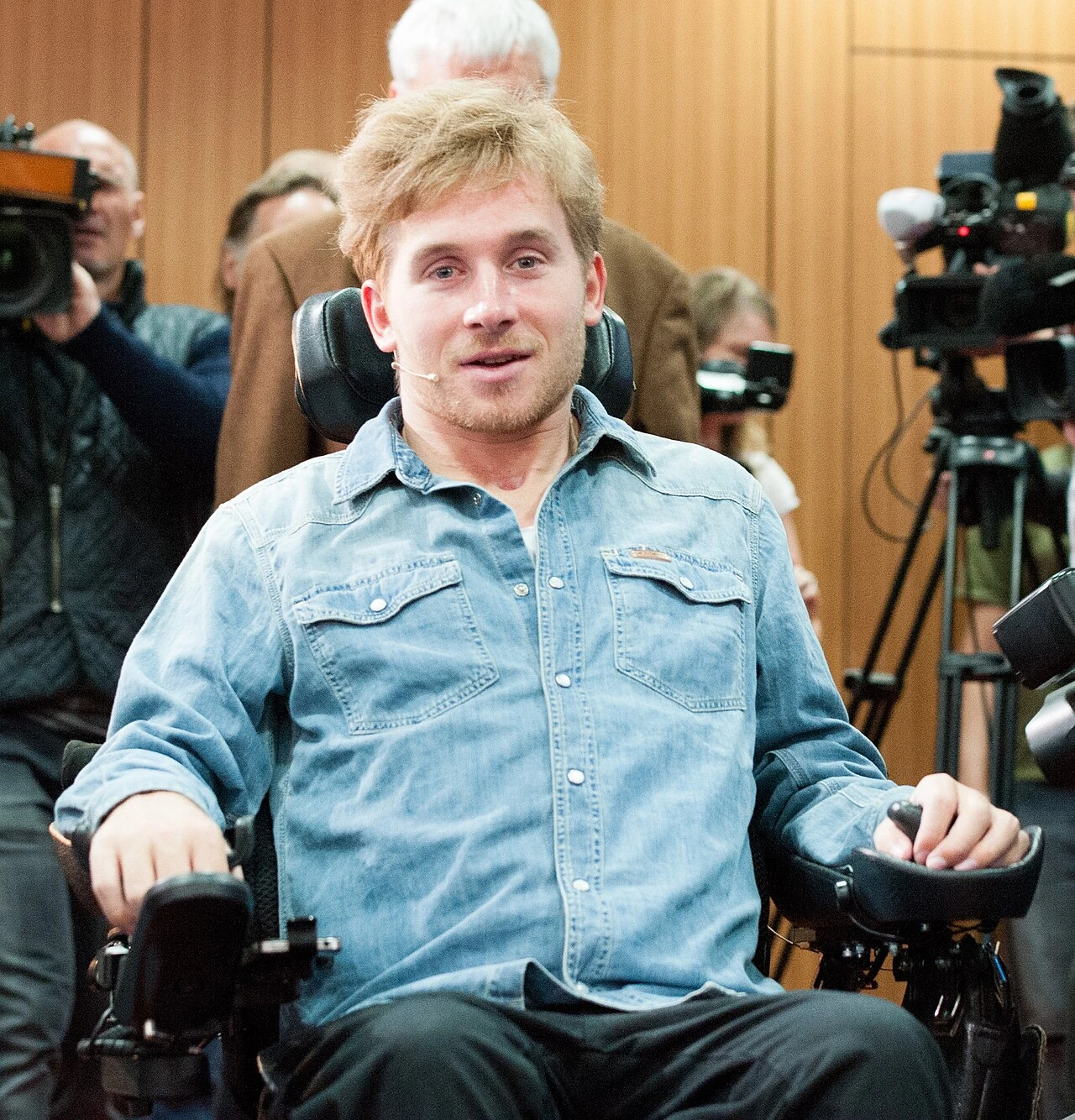 Samuel Koch seated in a wheelchair during a public event, facing the camera