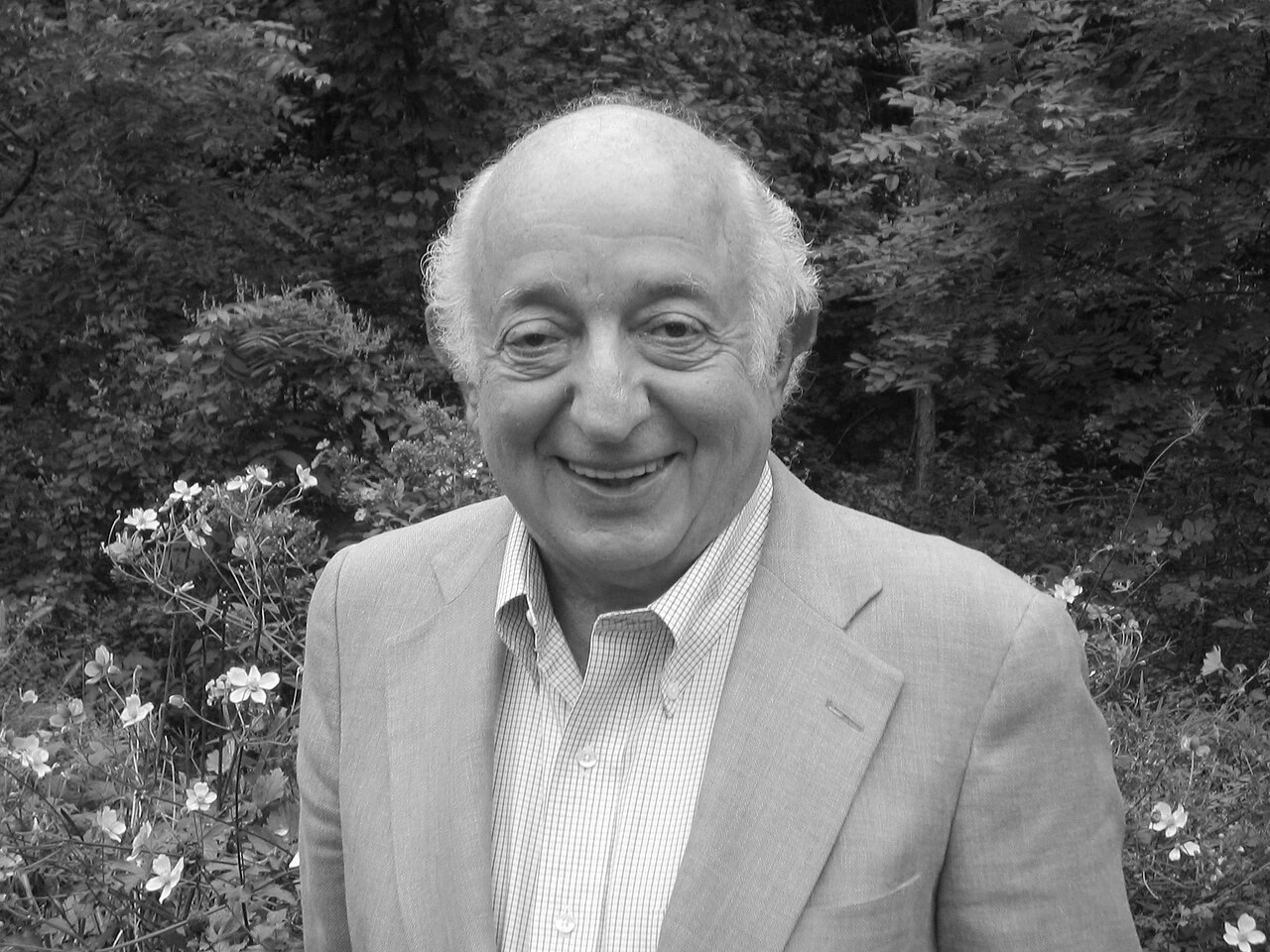 Black-and-white headshot of an older man smiling outdoors in a garden