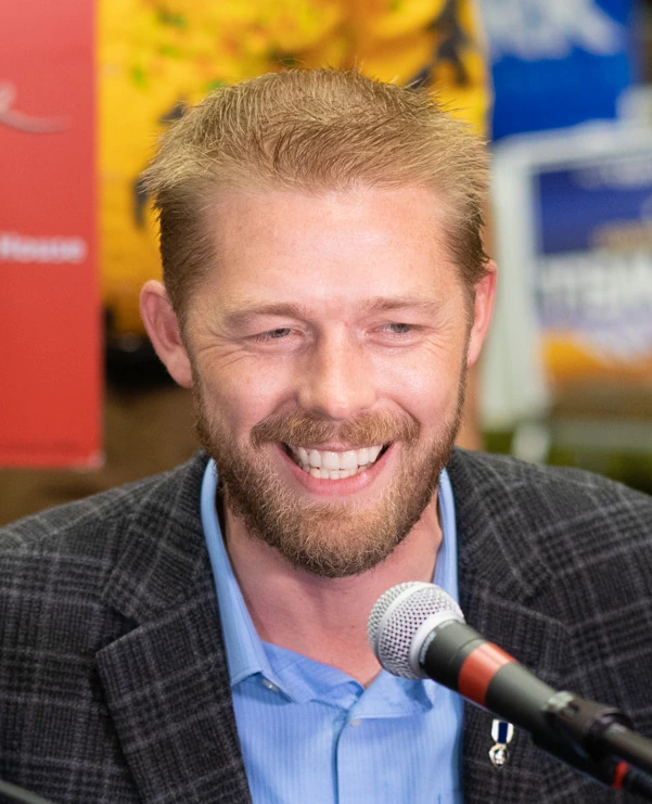 Portrait of Joshua Kozak speaking at a microphone