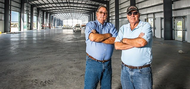 Two men standing with arms crossed inside a large industrial warehouse