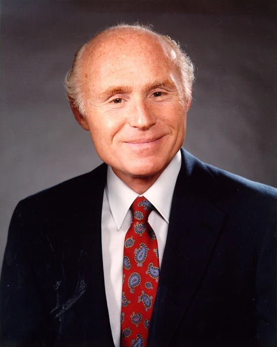 Portrait photo of Herb Kohl in a suit and red tie against a neutral background