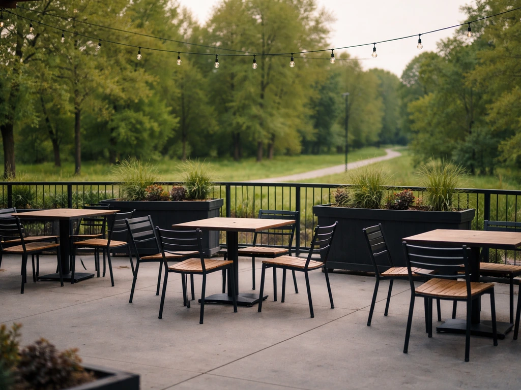Empty brewery patio with tables and chairs, looking out toward green trees of a nearby metro park.