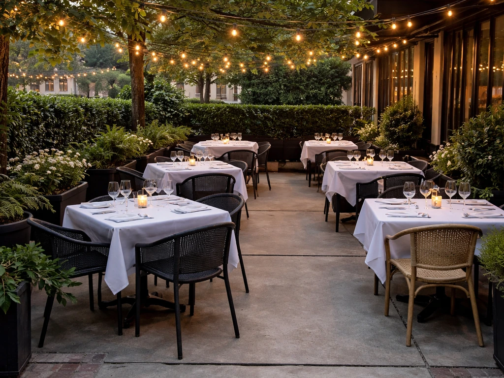 Elegant outdoor dining patio with neatly set tables, warm string lights, and potted greenery at a bistro.