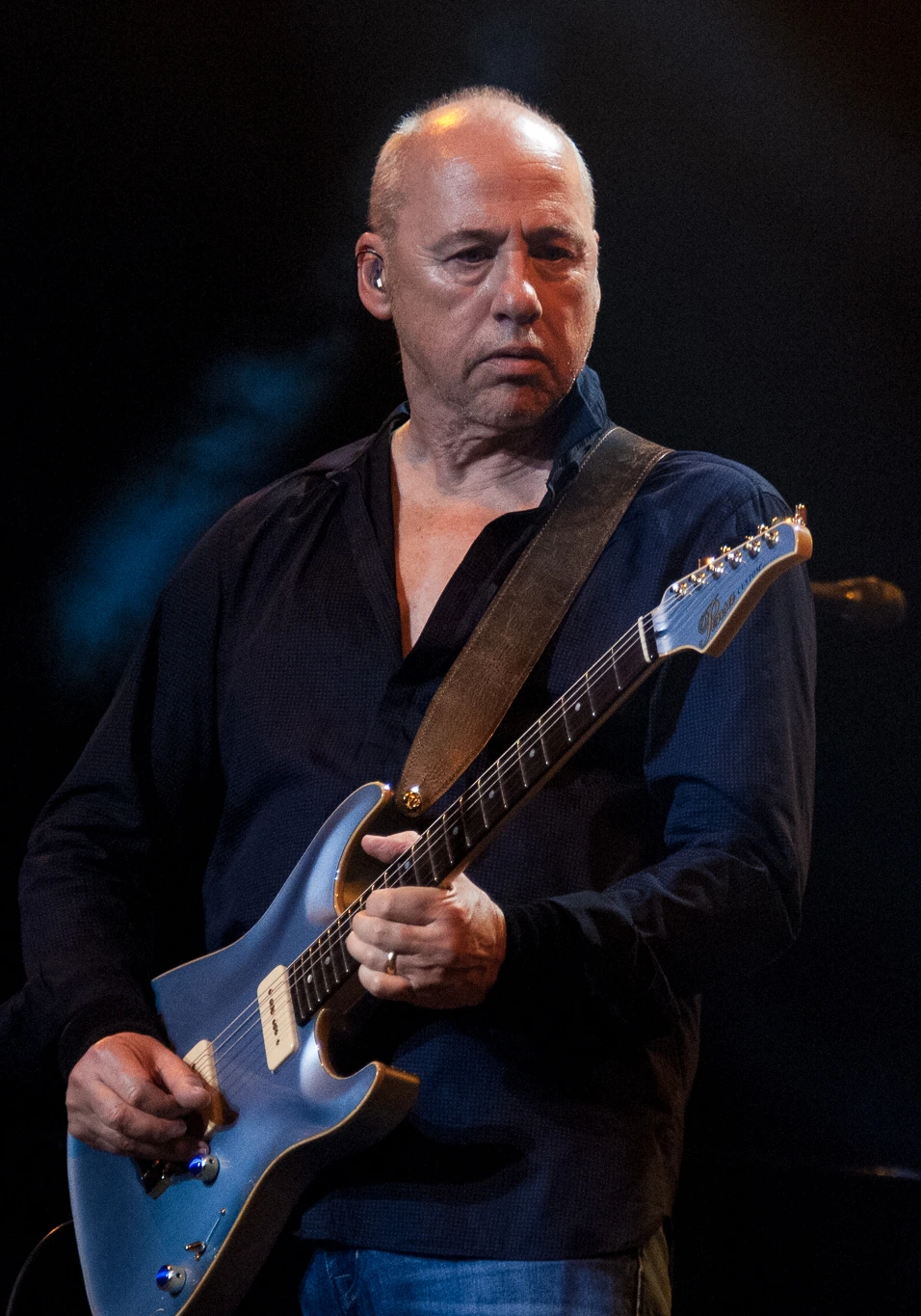 Mark Knopfler performing on stage with a blue electric guitar