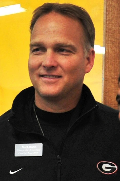 Mark Richt speaking at a Georgia Bulldogs event, wearing a black Georgia jacket