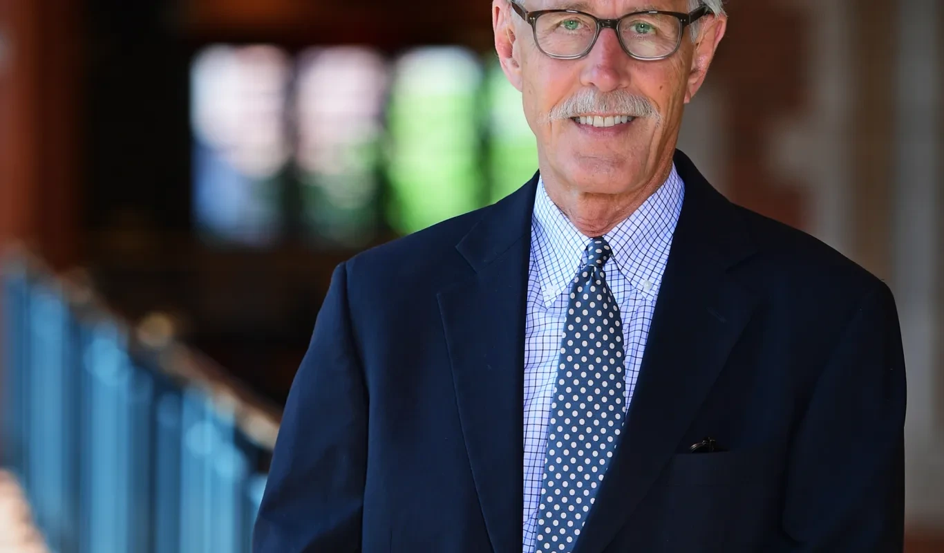 Portrait of Mark Rollins in a suit and tie, standing indoors and facing the camera.