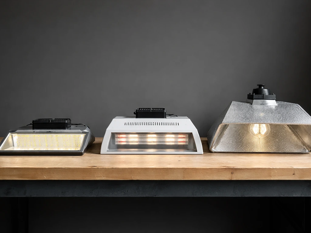 Three small grow light fixtures side-by-side, showing different hood/reflector styles on a workbench.