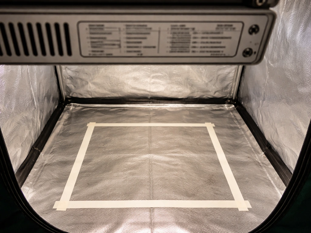 Close-up of an LED grow light specs area next to a taped-out canopy footprint inside a grow tent.