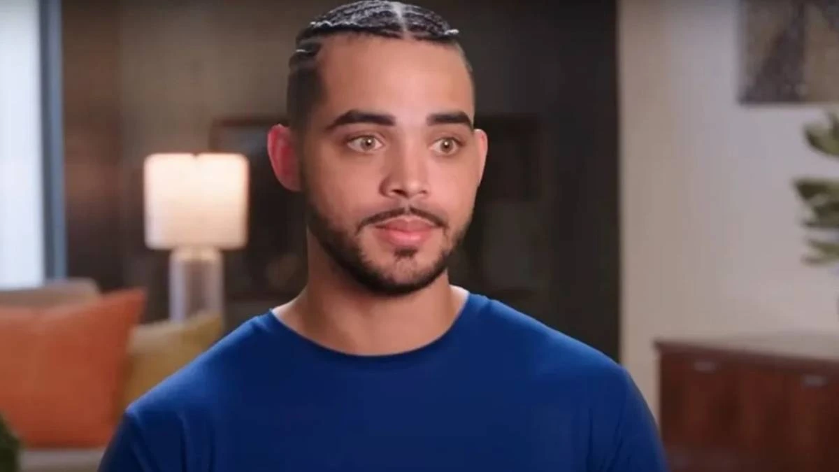 Rob Warne in a blue shirt, facing the camera in an indoor scene from 90 Day Fiancé.