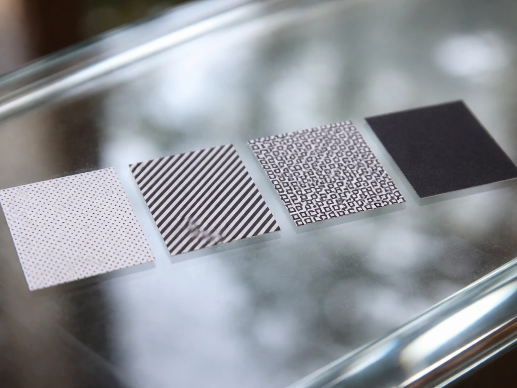 Macro photo of repeating geometric decal patterns on clear glass, showing dense grids side-by-side.