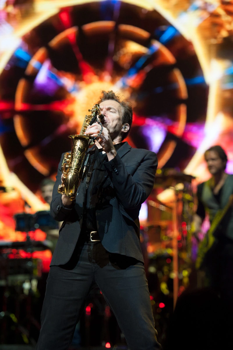 Ray Herrmann performing on saxophone on stage with colorful concert lighting behind him