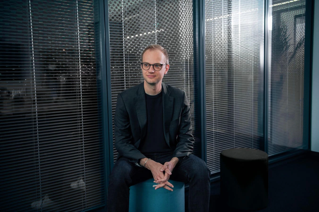 Alexander Rinke seated in a modern office setting, wearing glasses and a dark blazer.