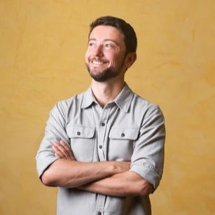 Portrait of Lenny Rachitsky standing with arms crossed against a plain yellow background.