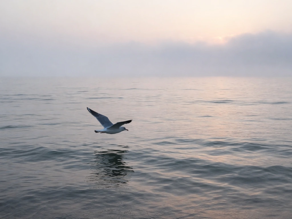 Misty sunrise over ocean with a single seagull flying above the waterline