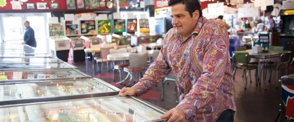 Robert J. Ilvento standing at a pinball machine inside an arcade museum, looking at the game in a casual documentary-sty