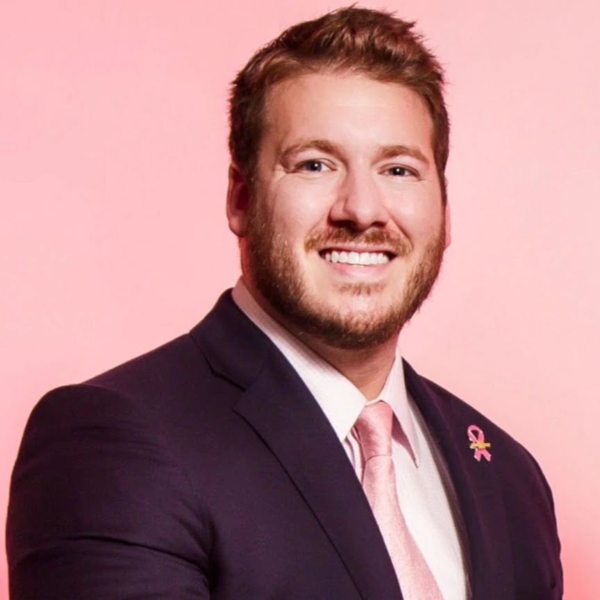 Portrait of Grant Navarre in a suit against a pink background
