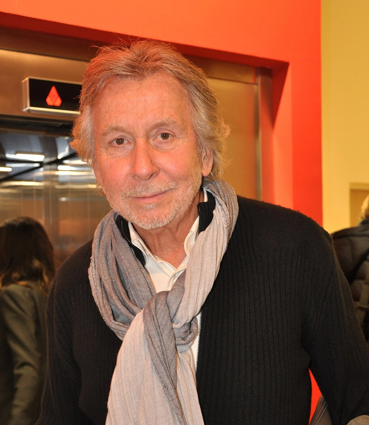 Portrait photo of Bernar Venet indoors wearing a scarf and dark sweater.