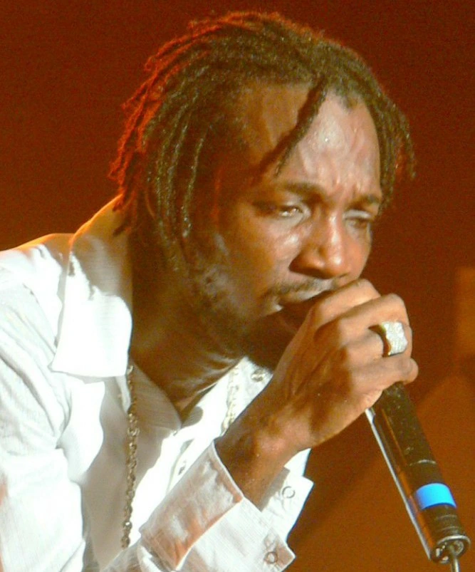 Mavado performing on stage, holding a microphone and wearing a white shirt