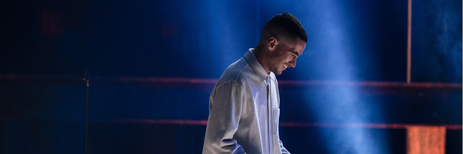 Ricky Velez smiling on stage under blue lighting
