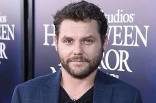 Jason James Richter at a red carpet event, wearing a dark jacket and standing in front of a promotional backdrop.