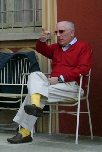 Peter S. Kalikow seated outdoors in a red sweater and sunglasses, gesturing with his hand.