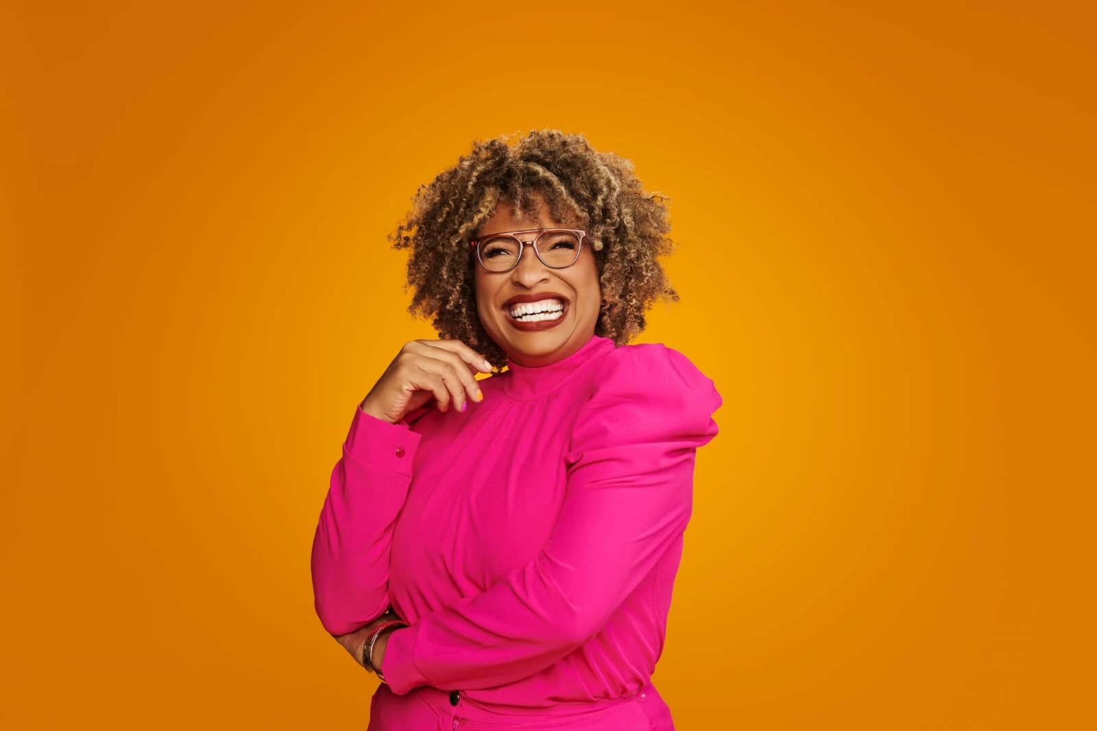 Portrait of Mignon Francois smiling in a bright pink outfit against an orange background