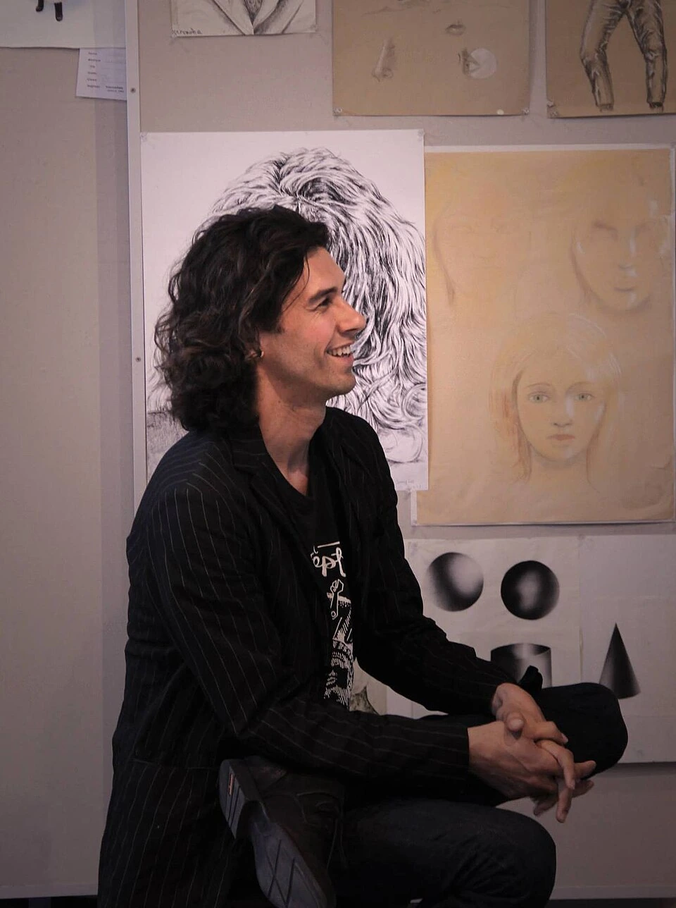 Tom Franco seated in an art studio, smiling in profile with artwork displayed behind him
