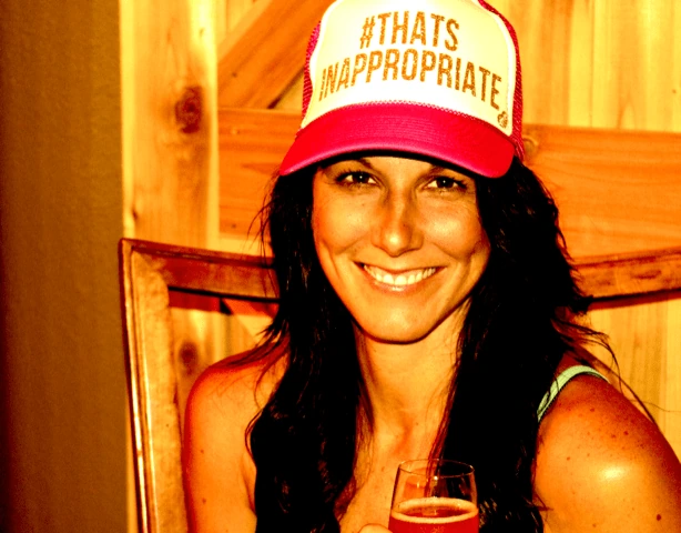 Meredith Masony smiling in a casual portrait, wearing a '#THAT'S INAPPROPRIATE' hat.
