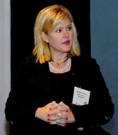 Meredith Whitney speaking at an event, wearing a black outfit and pearl necklace