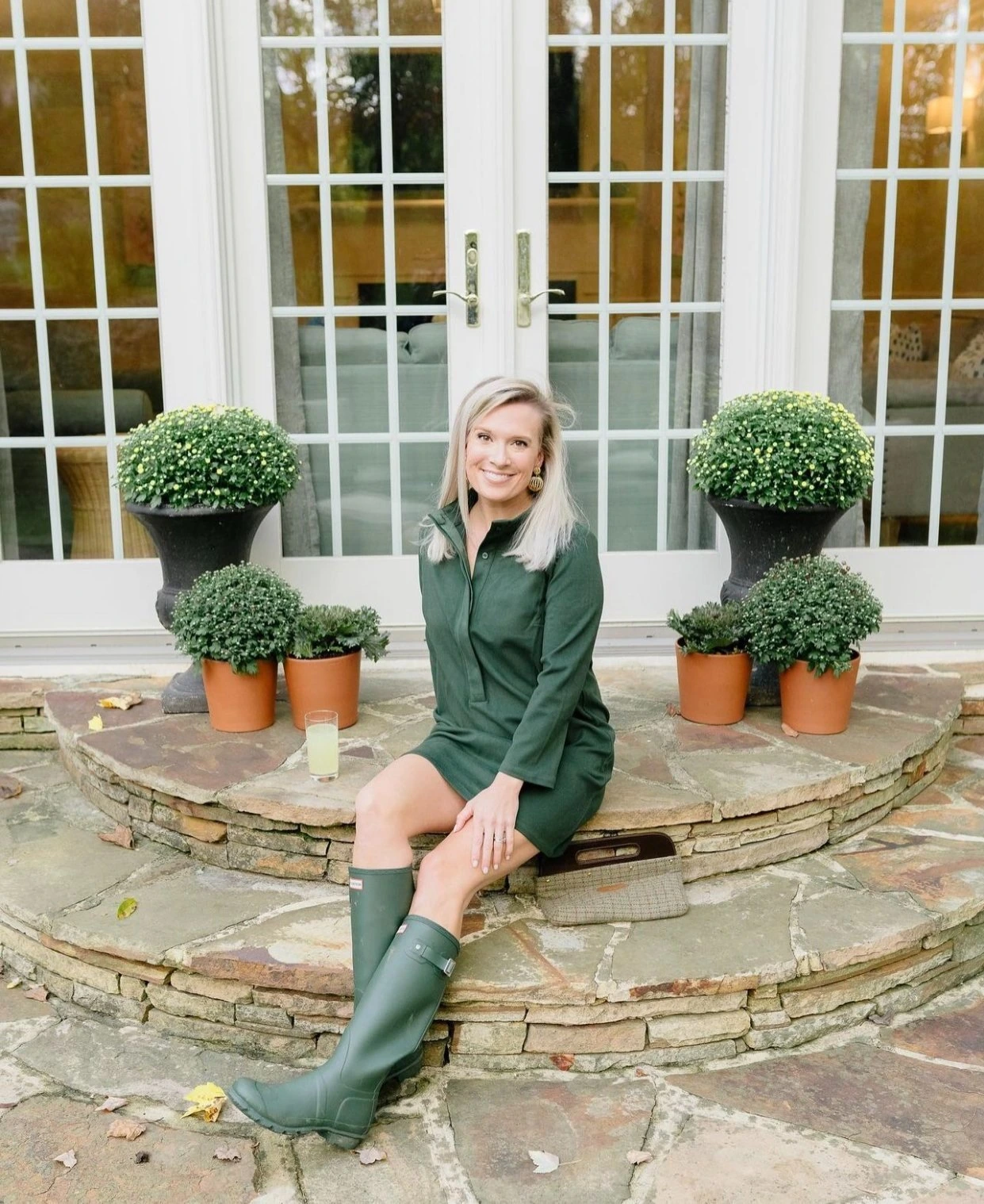 Meredith Hudkins seated outdoors in a green dress and rain boots on a stone patio