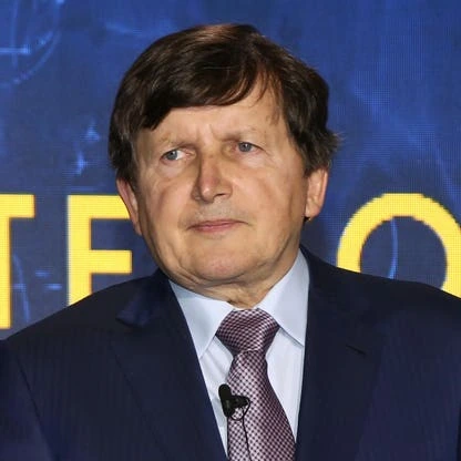 Portrait photo of Charles Simonyi in a suit and tie against a blue event backdrop.