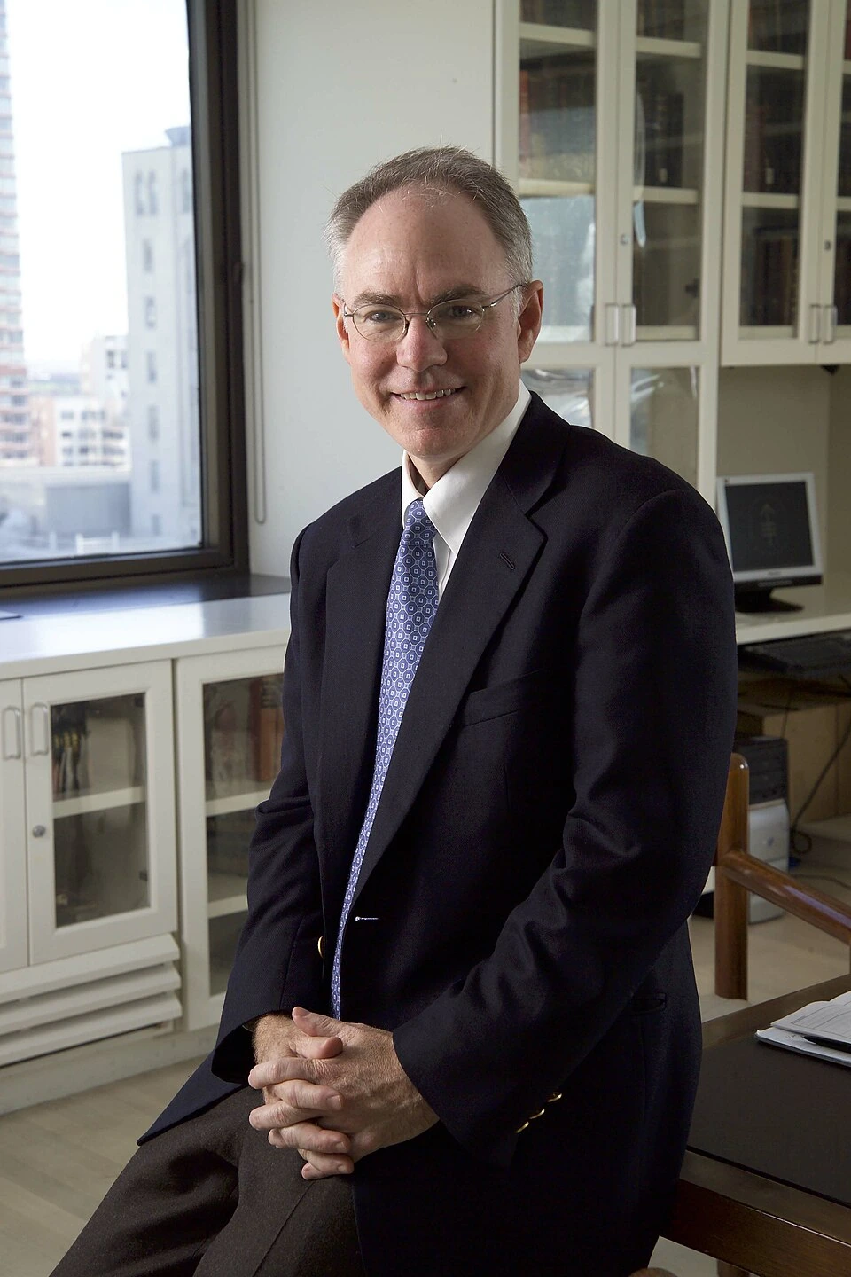Charles L. Sawyers seated in an office wearing a suit and tie, smiling at the camera.