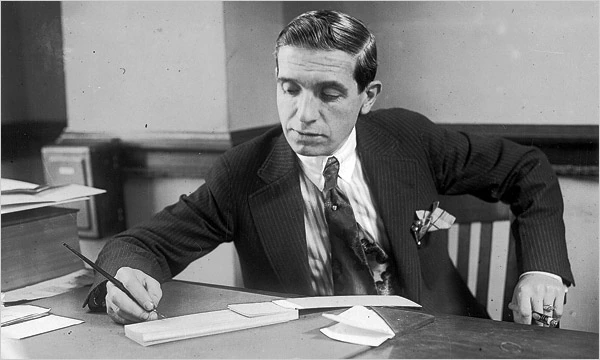 Black-and-white portrait photo of Charles Ponzi seated at a desk, writing with a pen