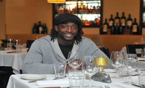 Charles Tillman seated at a dining table in a restaurant, smiling at the camera