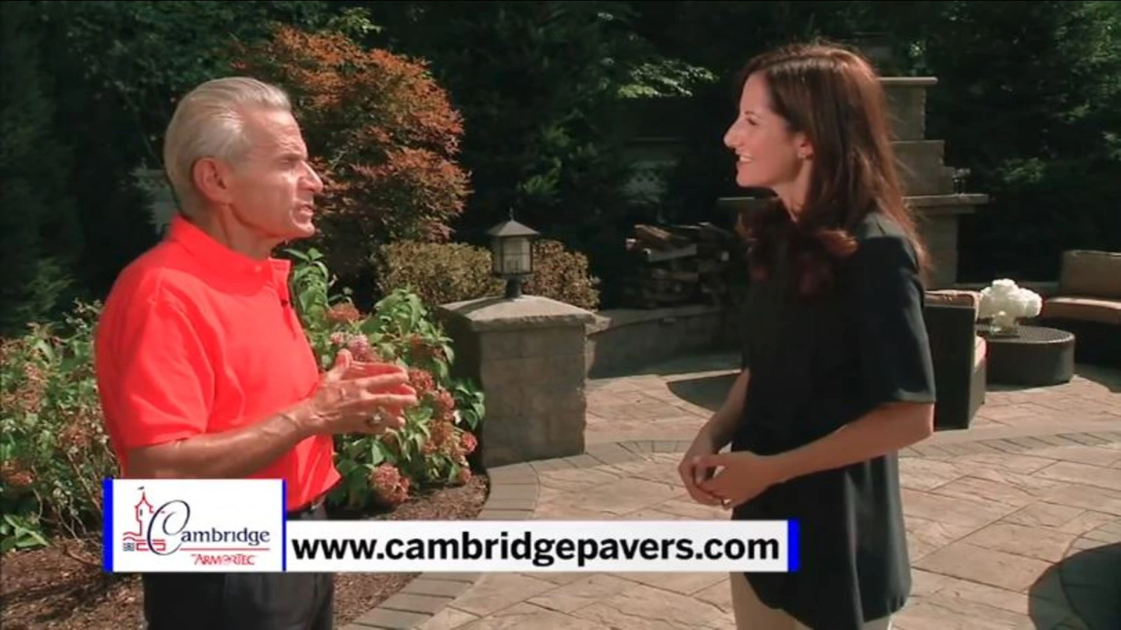Charles H. Gamarekian speaking outdoors in a Cambridge Pavers feature segment, standing beside a woman in a landscaped p
