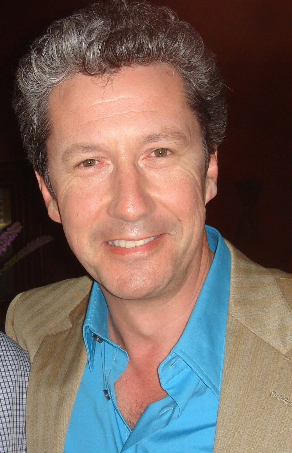 Portrait of Charles Shaughnessy smiling in a blue shirt and tan jacket