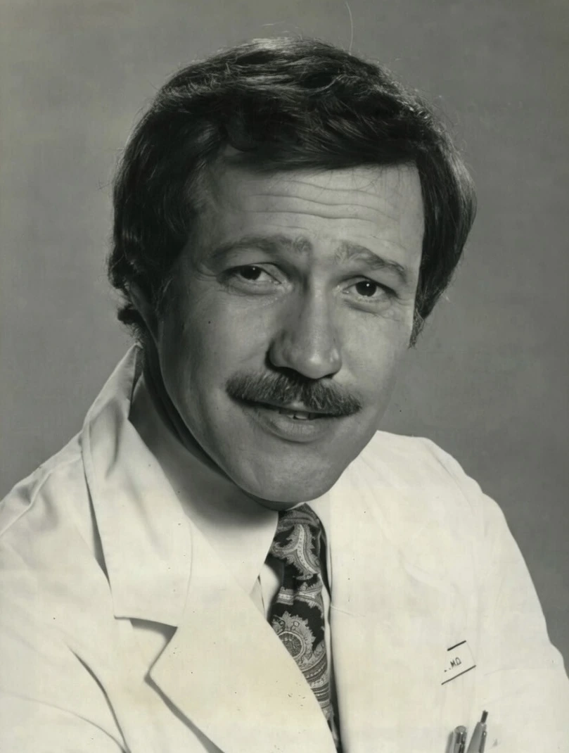 Charles Alan Siebert in a 1979 press photo for Trapper John, M.D., wearing a doctor’s coat and tie.