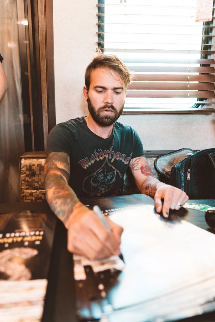 Charles Trippy seated at a table signing or writing on a page, indoors.